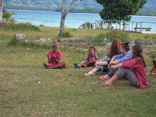 Pele Island and Kindlehill children foster communal connection through shared stories, sitting together beside the tropical sea.