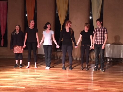 Students stand together on stage, holding hands to celebrate the courage and connection of sharing their original voices.