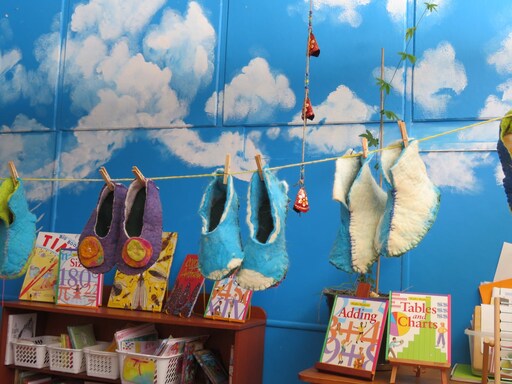 Hand-felted slippers hang before a sky-painted wall, embodying the creative heart and warm spirit of community.