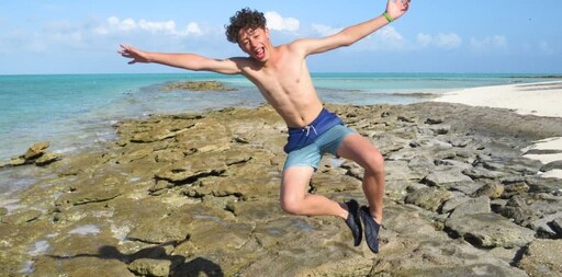 A joyful student leaps on the shore, embracing an earth-centred connection to the vibrant life of the reef.