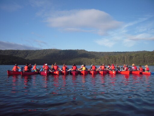 Students in red canoes link hands, embodying connection, community, and resilience through outdoor learning in the Australian bush.
