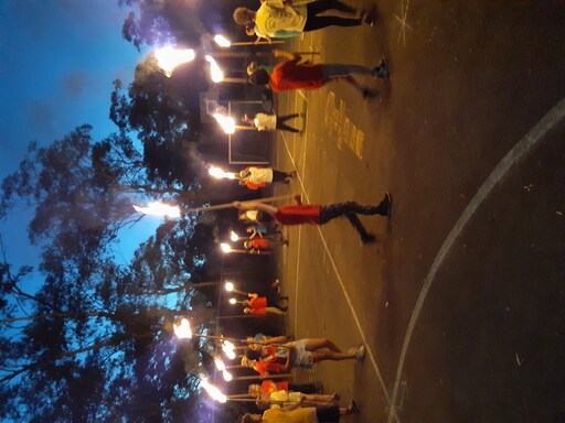 Sunshine Class students perform a rhythmic fire staff routine, demonstrating resilience and creative connection under the evening sky.
