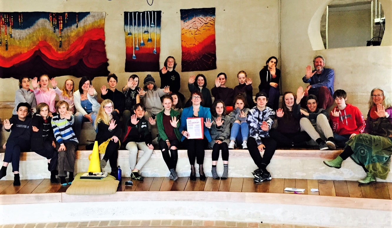 Kindlehill students and teachers raise palms in solidarity, advocating for social justice amidst vibrant, handcrafted colourful tapestries.