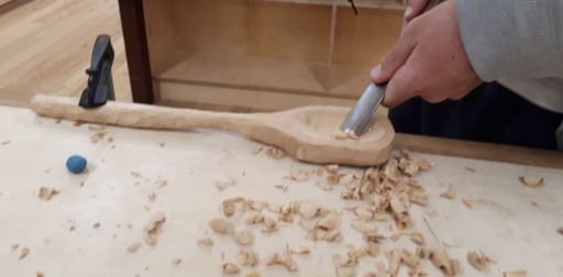 Hands mindfully carve a wooden spoon at Kindlehill, connecting head, heart, and hands through artistic, earth-centred craftsmanship.
