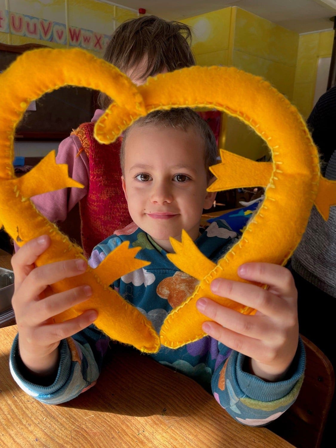 A Kindlehill student frames his smile with a heart-shaped felt skink, representing nature-centred learning and artistic connection.