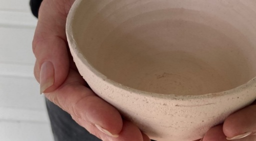 Hands cradle a rustic ceramic bowl, honouring the sustainable link between traditional craft, local resources, and personal purpose.