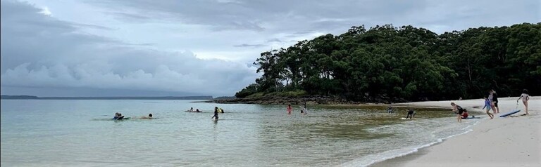 Students swim and play on a coastal beach, building resilience and connection beneath an atmospheric, rain-filled sky.