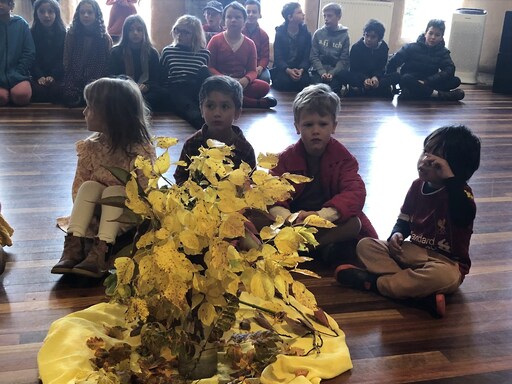 Children gather around golden autumn leaves, honouring seasonal rhythms and the warm spirit of their school community.
