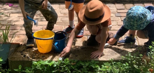 Children collaborate with brushes and water, cultivating a sense of contribution and reverence in their nature-centred outdoor space.