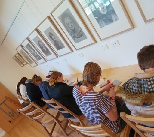 Focused students refine their creative voices and writing skills beneath artistic portraits in a communal Kindlehill learning space.