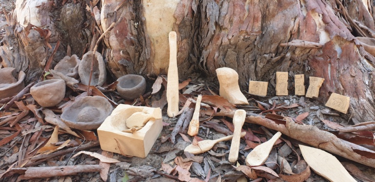 Handcrafted student pinch pots and wood carvings nestled against a gum tree at an exhibition on Wiradjuri Country.