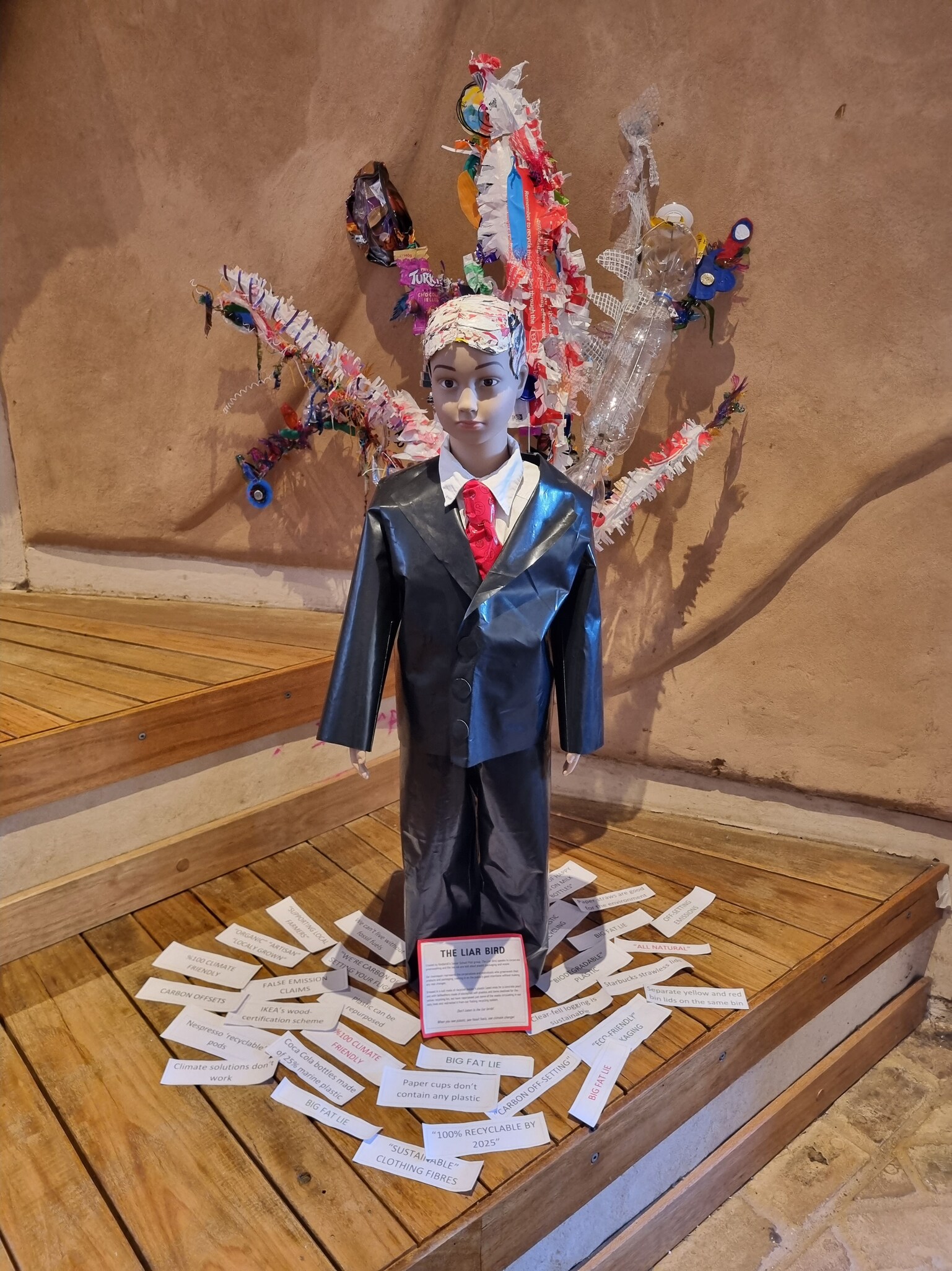 The Liar Bird sculpture critiques corporate greenwashing using a plastic-suited mannequin and colourful repurposed plastic waste tailfeathers.
