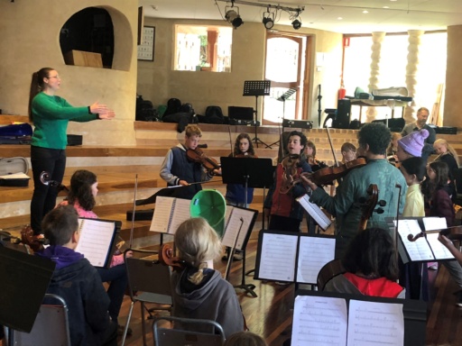 Children from local schools collaborate in a combined orchestra, fostering community spirit through shared musical expression and creativity.