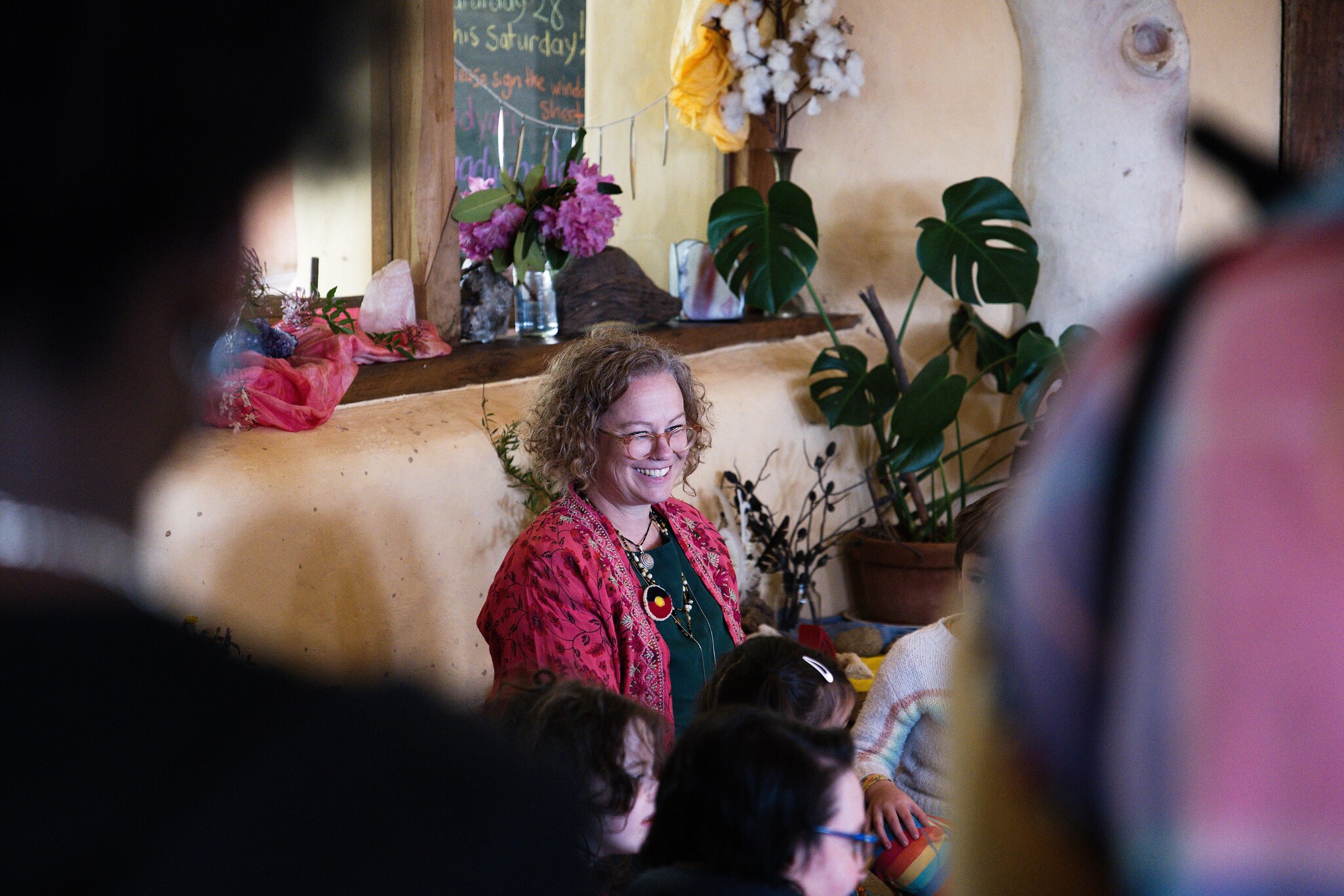 A teacher smiles warmly at children in an earthy room, illustrating Kindlehills heart-centred community connection and joy.