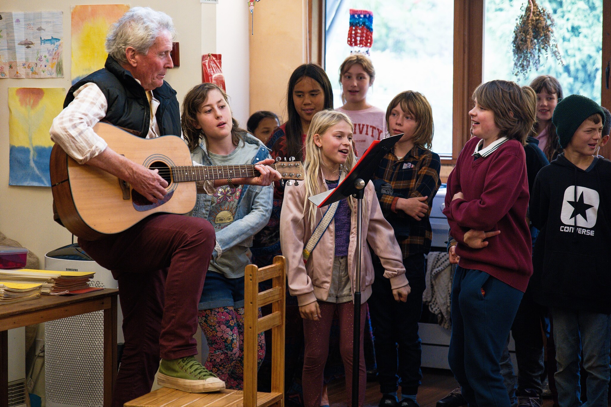 Kindlehill students sing alongside an elder, threading hearts with wonder and community spirit through shared musical expression.