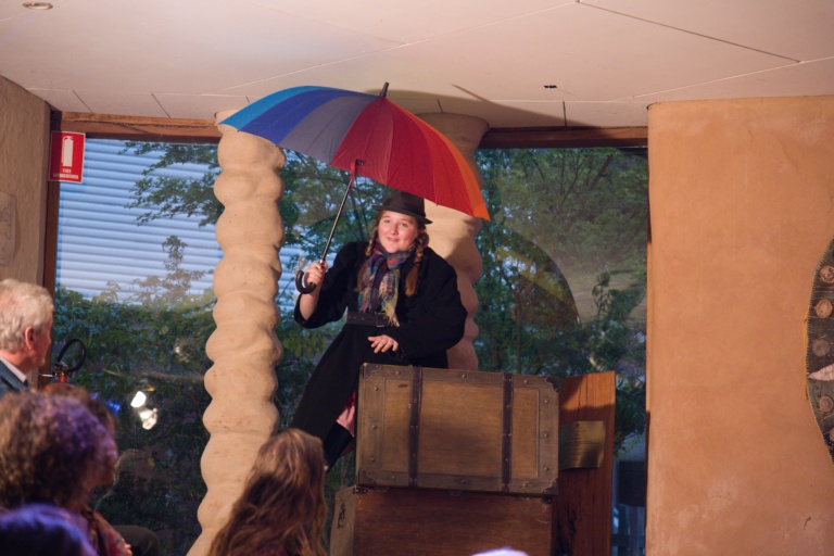 A student performer holding a colourful umbrella embodies courage and heart through whimsical storytelling and creative community expression.