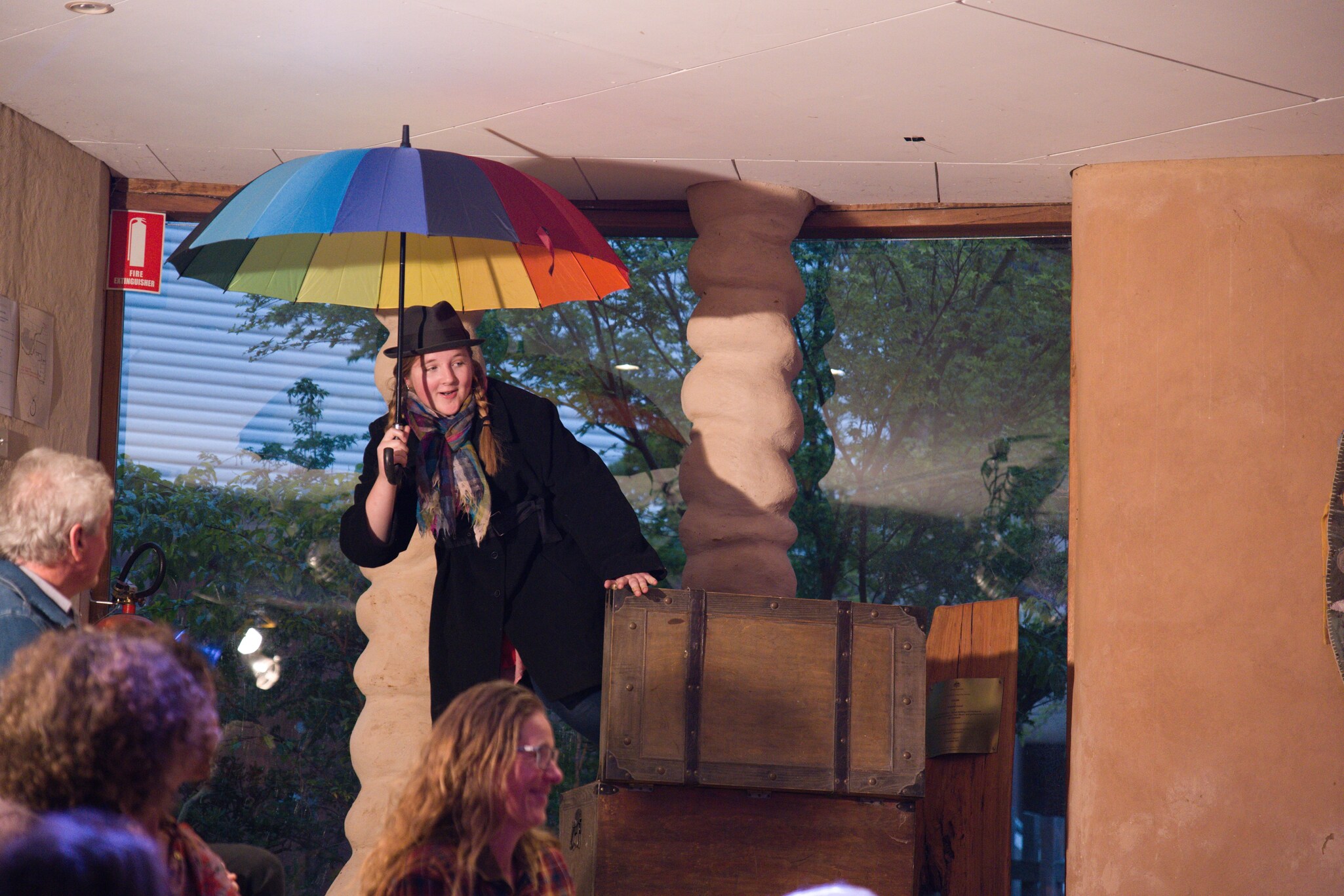 A student holding a rainbow umbrella atop a chest embodies imagination, heart, and courage during a Kindlehill performance.
