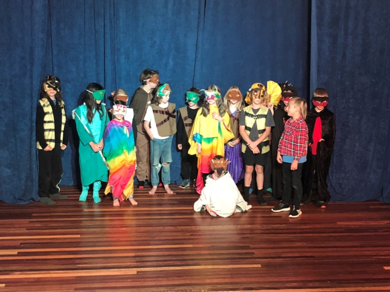 Kindlehill students in colourful masks and costumes collaborate on stage, celebrating individual expression and collective community spirit.