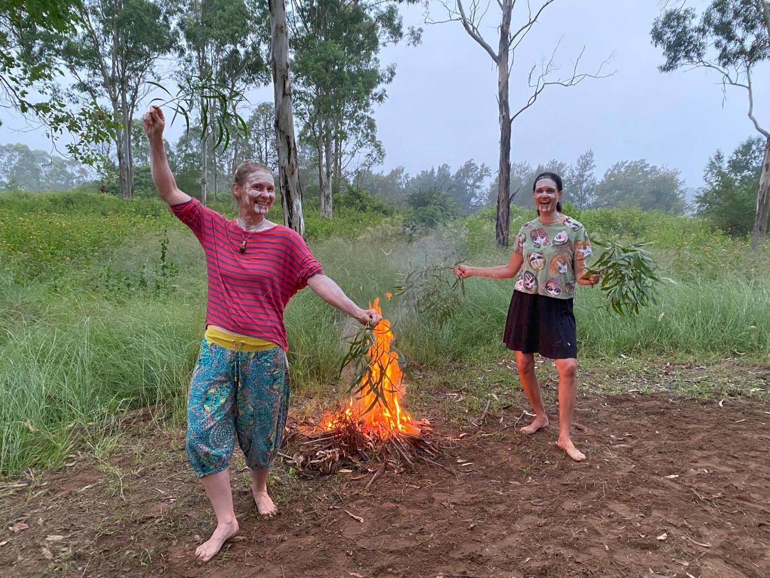 Parents participate in cultural ceremony, honouring Country and community spirit around a campfire in the bush.