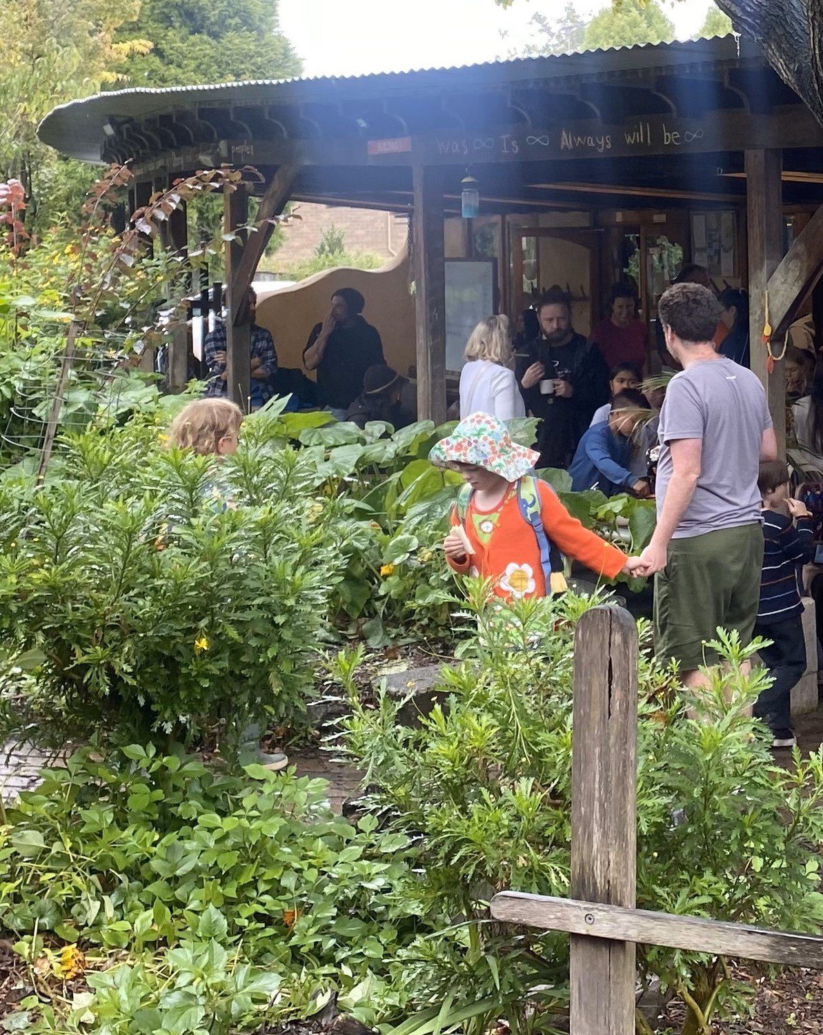 Families share snacks and conversation amongst garden greenery, nurturing a warm sense of belonging and connection to land.
