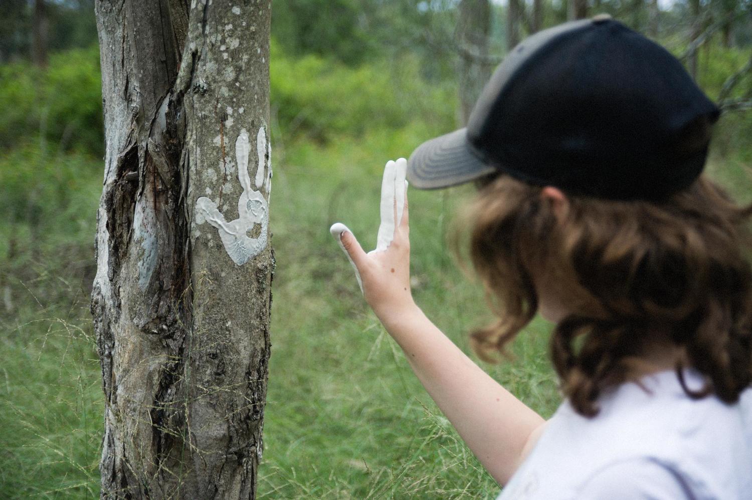 A student honours Country by placing their ochre-covered hand beside a white stencil on a Blue Mountains tree.
