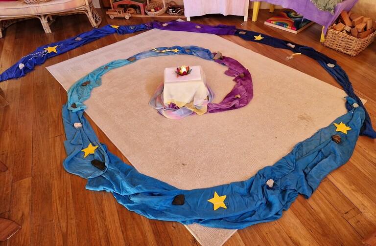 A silk spiral adorned with stars leads to a central candle, guiding playgroup children toward their inner light.