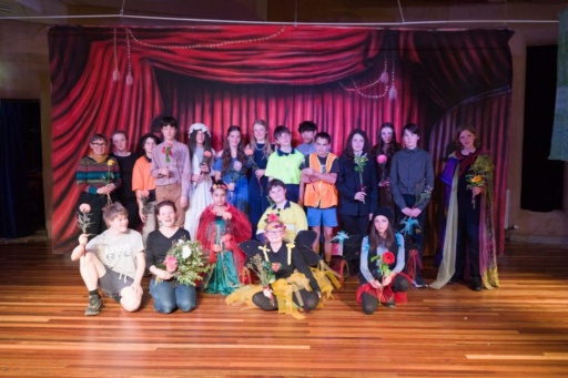 Kindlehill students and teachers celebrate their collaborative Shakespearean theatre performance on stage, holding flowers and showcasing community spirit.
