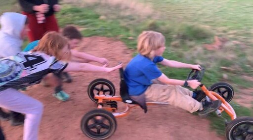 Children collaboratively launch a billy cart down a dirt hill, embracing the exhilaration and connection of risky play.