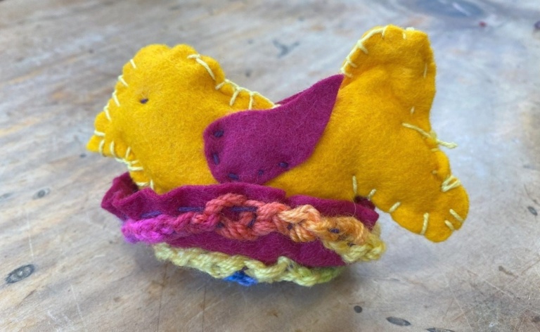 Hand-stitched felt bird in a colourful woollen nest reflecting the patient, creative rhythm of heart-centred learning.
