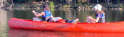 Students navigate a red canoe across calm waters, building resilience and strength through shared connection with the land.