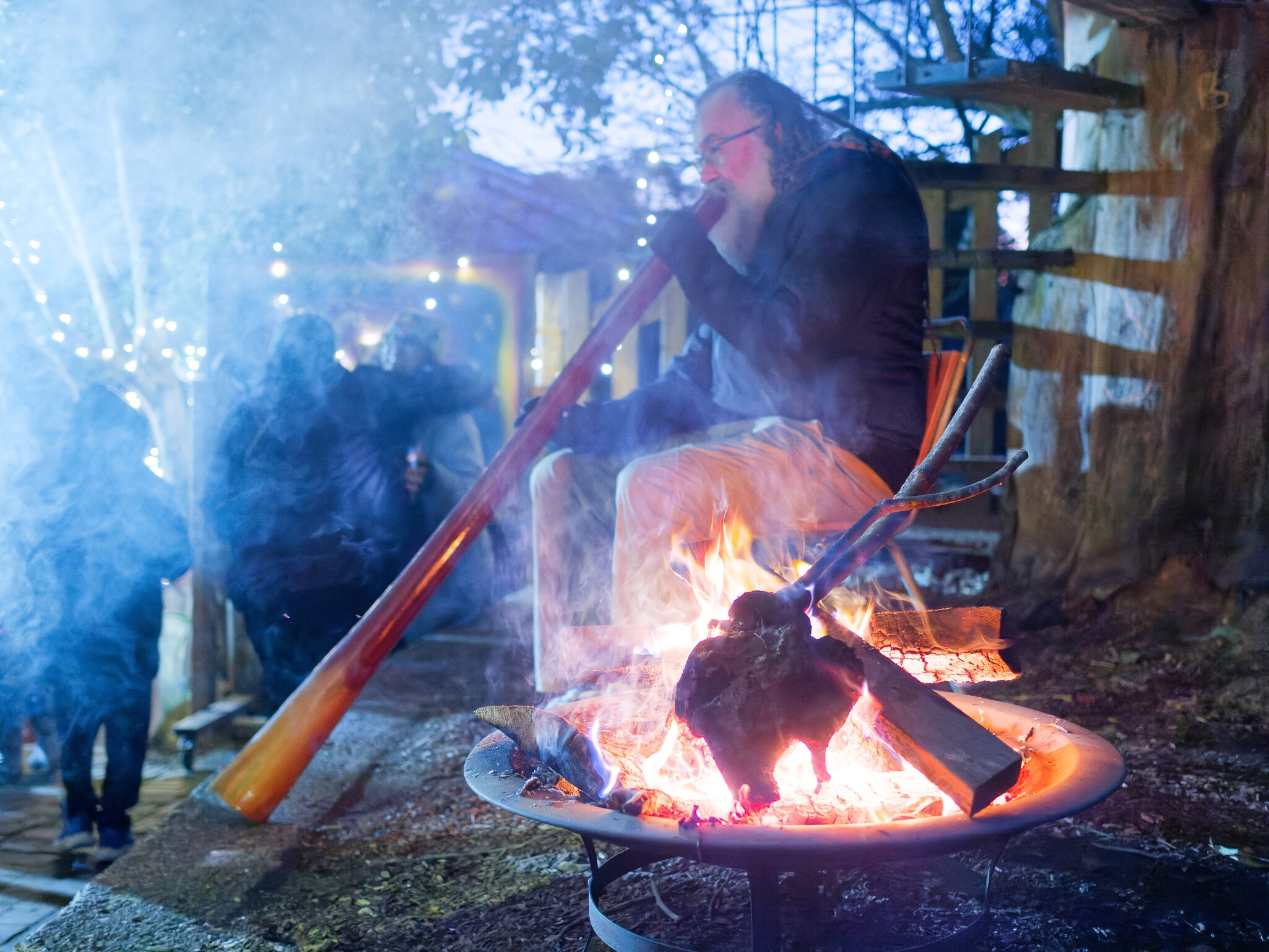An Elder plays the didgeridoo by a glowing fire, honouring Country and light during a sacred winter ritual.