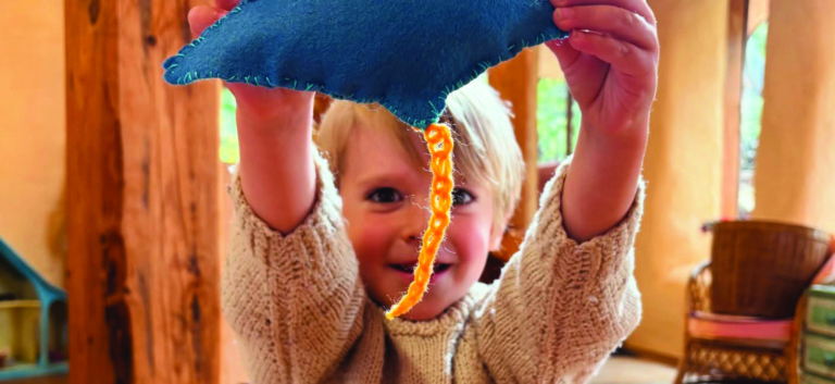 A Kindy child proudly displays their handcrafted blue felt bird, embodying imagination and learning through head, heart, and hands.