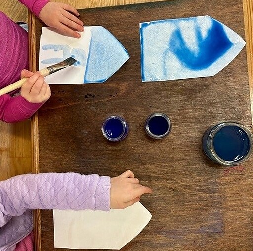 Childrens hands paint blue lanterns, illustrating artistic expression and communal rhythm during the Kindlehill after-school programme.