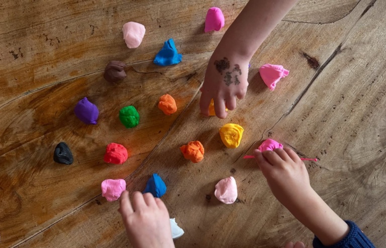 Children share colourful dough on a timber table, fostering connection and creative rhythm through nurturing, tactile play.