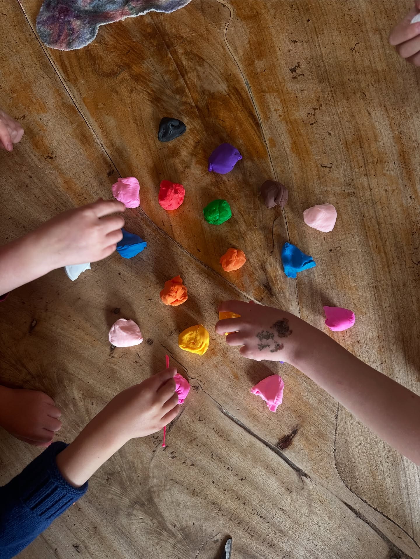 Childrens hands shape colourful clay together on a timber table, building community connection through creative and tactile play.