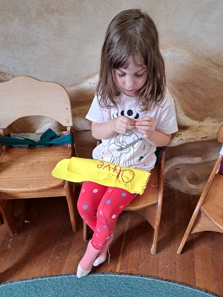 A student hand-sews her name, honouring her developmental journey through a rhythmic connection of head, heart, and hands.