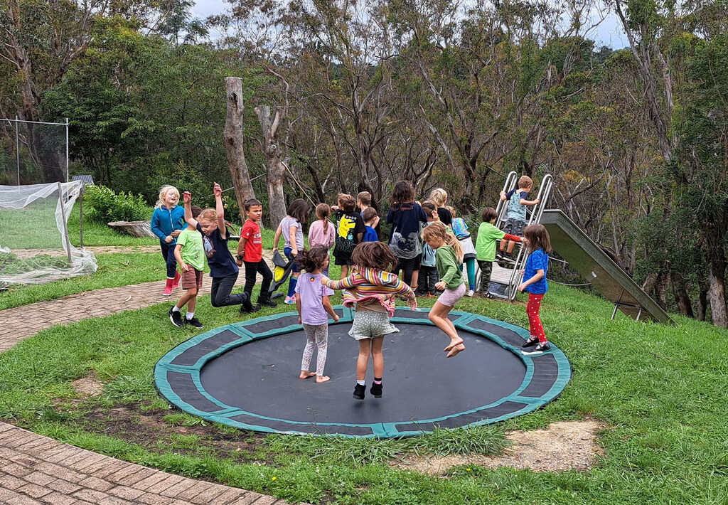 Children jump together outdoors, fostering community spirit and a deep connection to the ancient Blue Mountains landscape.