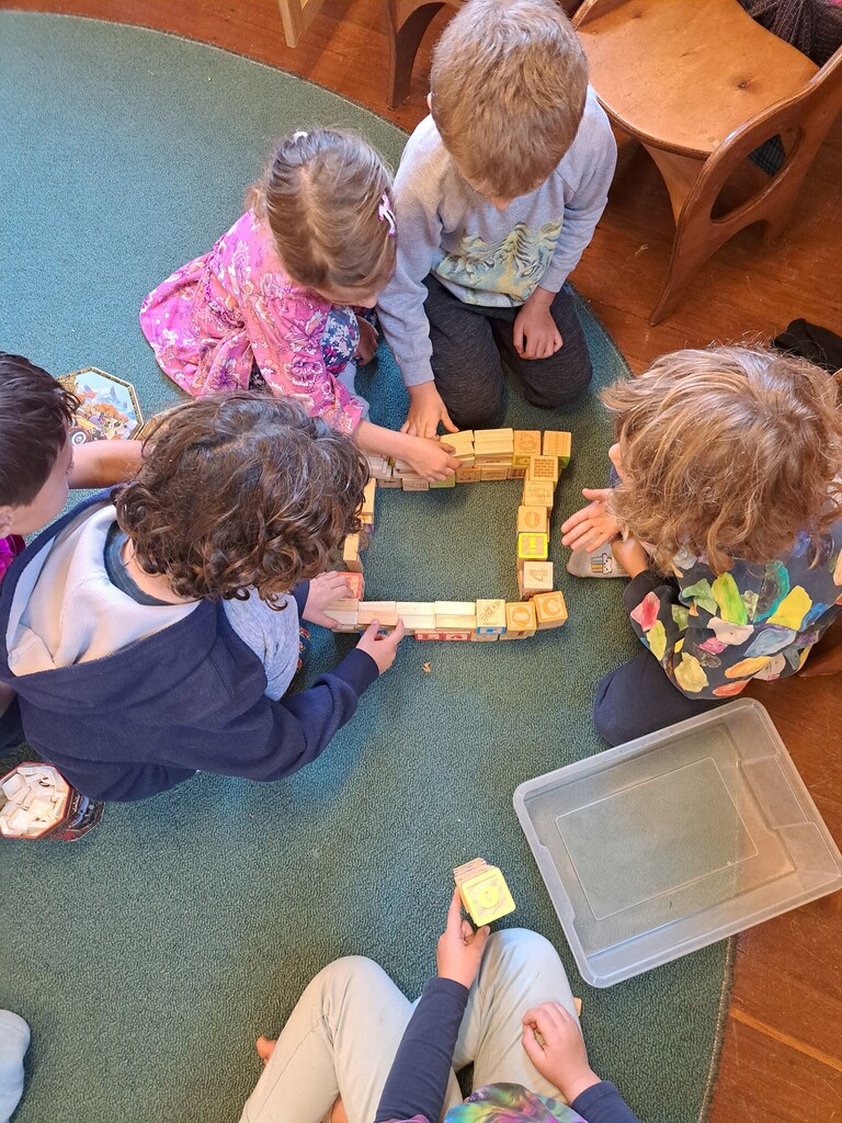 Kindlehill students cultivate community and imagination while building together with natural wooden blocks on a shared rug.