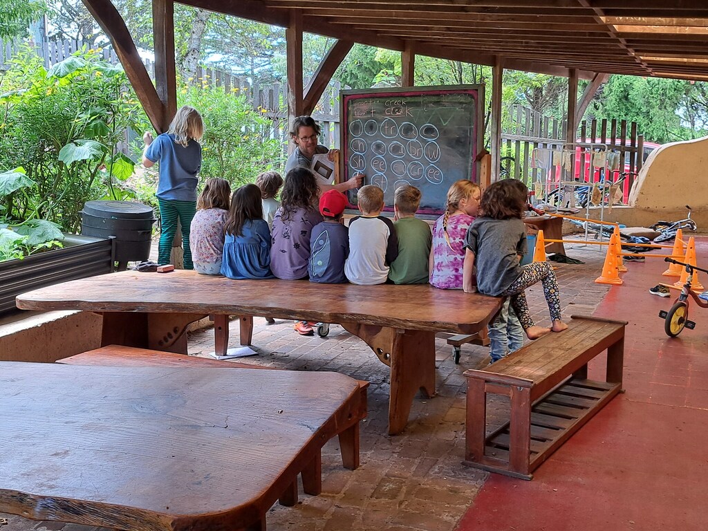 Students gather on a timber table, honouring natures rhythmic lessons within a bush-centred outdoor classroom.