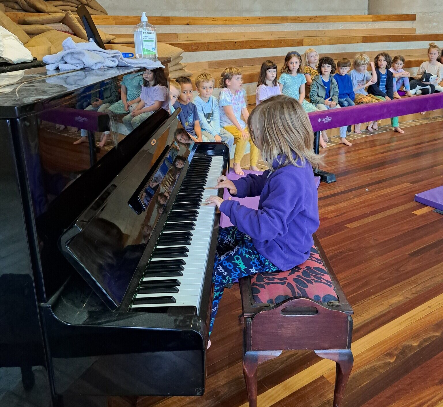 Students listen intently as a classmate plays piano, honouring artistic expression and the shared spirit of community.