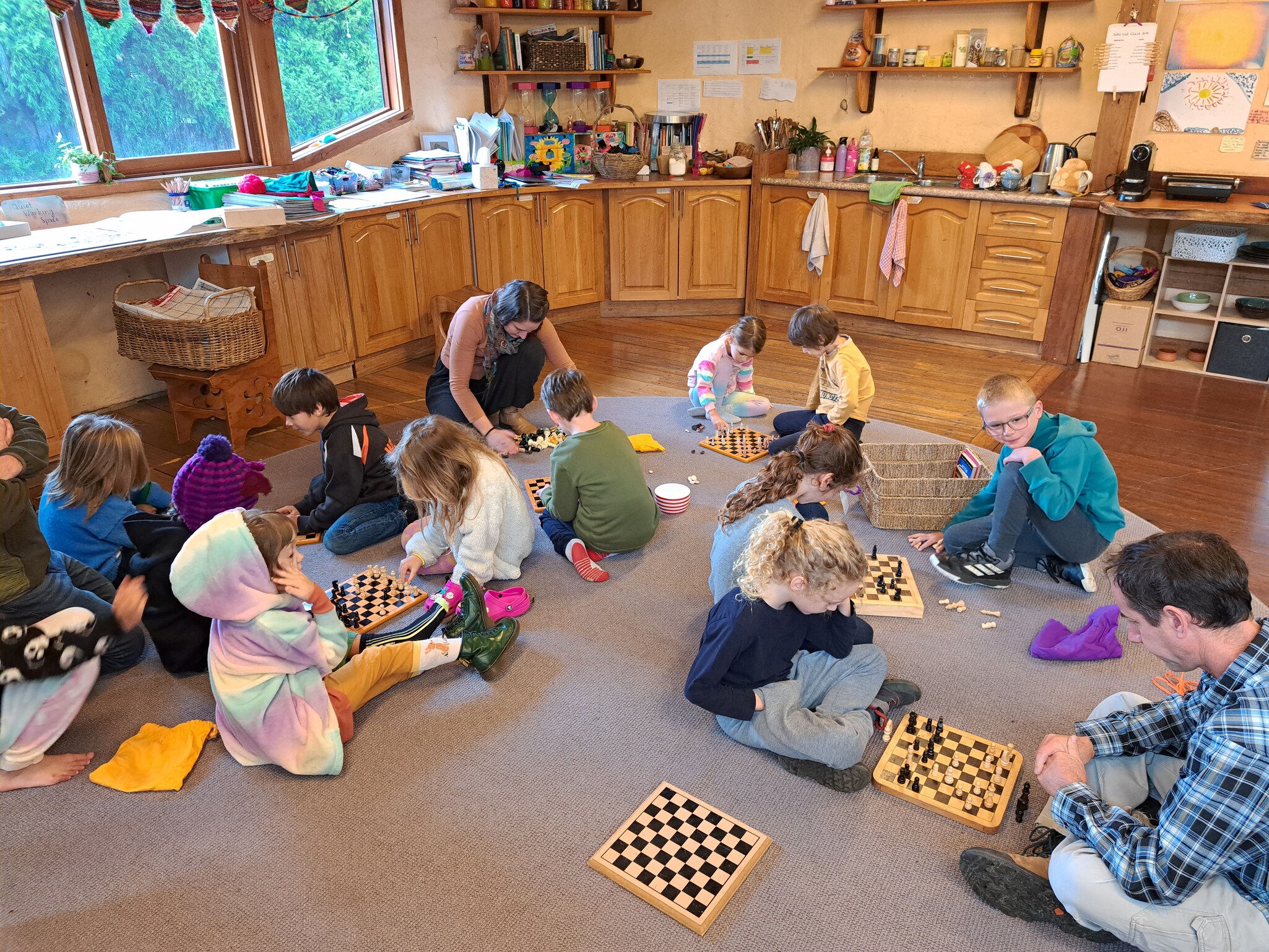 Kindlehill children and adults foster social connection and community spirit through shared strategic play in the classroom hearth.