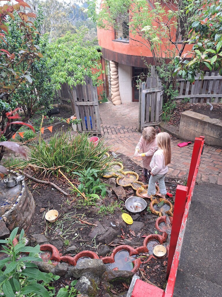 Barefoot children discover the rhythm of water and earth, cultivating wonder within Kindlehills lush garden environment.