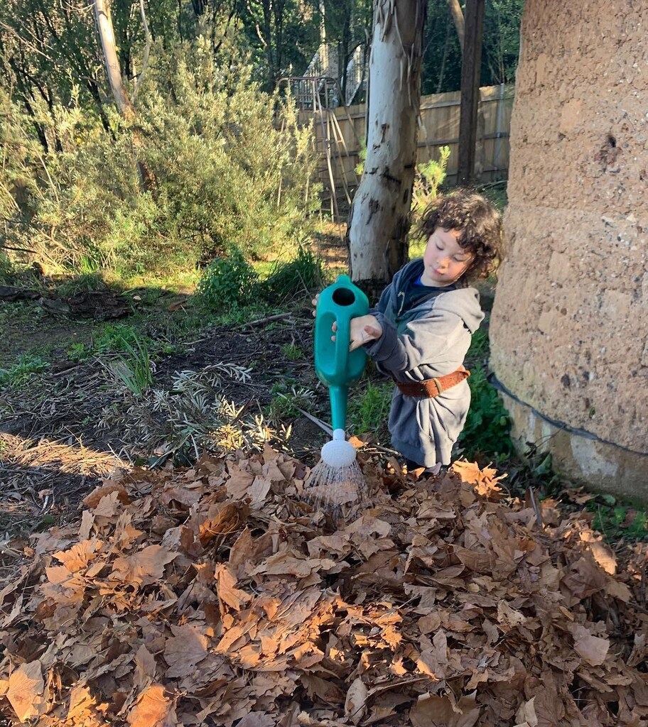 A student waters autumn leaves, nurturing the soil through biodynamic composting to honour the Earths natural seasonal rhythms.