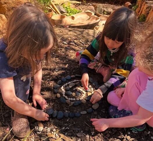Children collaboratively create a stone spiral, fostering connection to the land and cultivating wonder through rhythmic, hands-on learning.