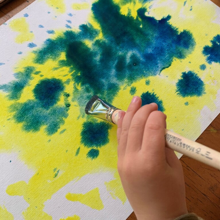 A childs hand paints with vibrant watercolours, expressing imagination and connection to nature through heart-centred artistic flow.