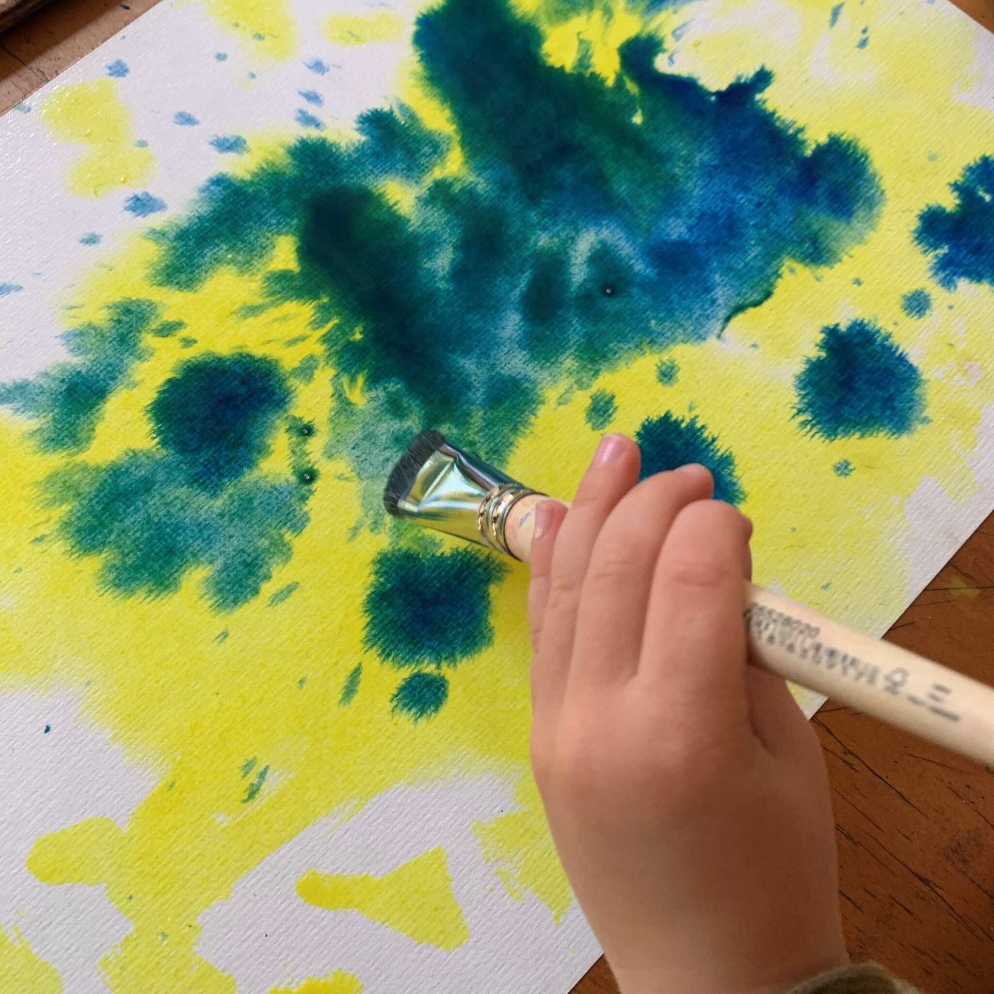 A childs hand paints with vibrant watercolours, expressing imagination and connection to nature through heart-centred artistic flow.