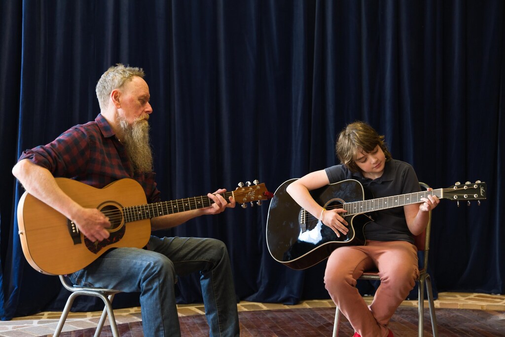 A teacher and student build connection through shared music, honouring artistic expression and the rhythmic spirit of community.