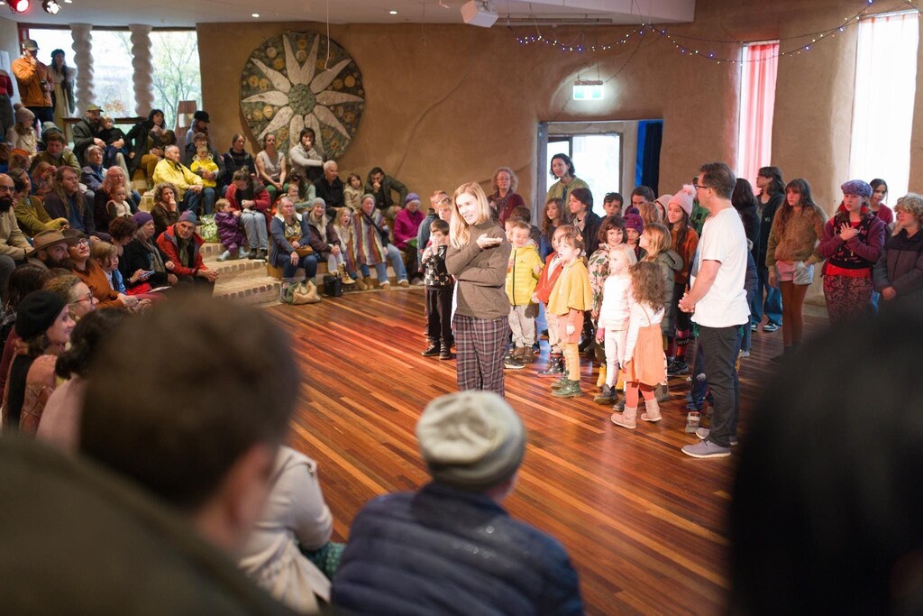 Kindlehill families gather in the earthen hall to sing, building a village through connection and shared purpose.