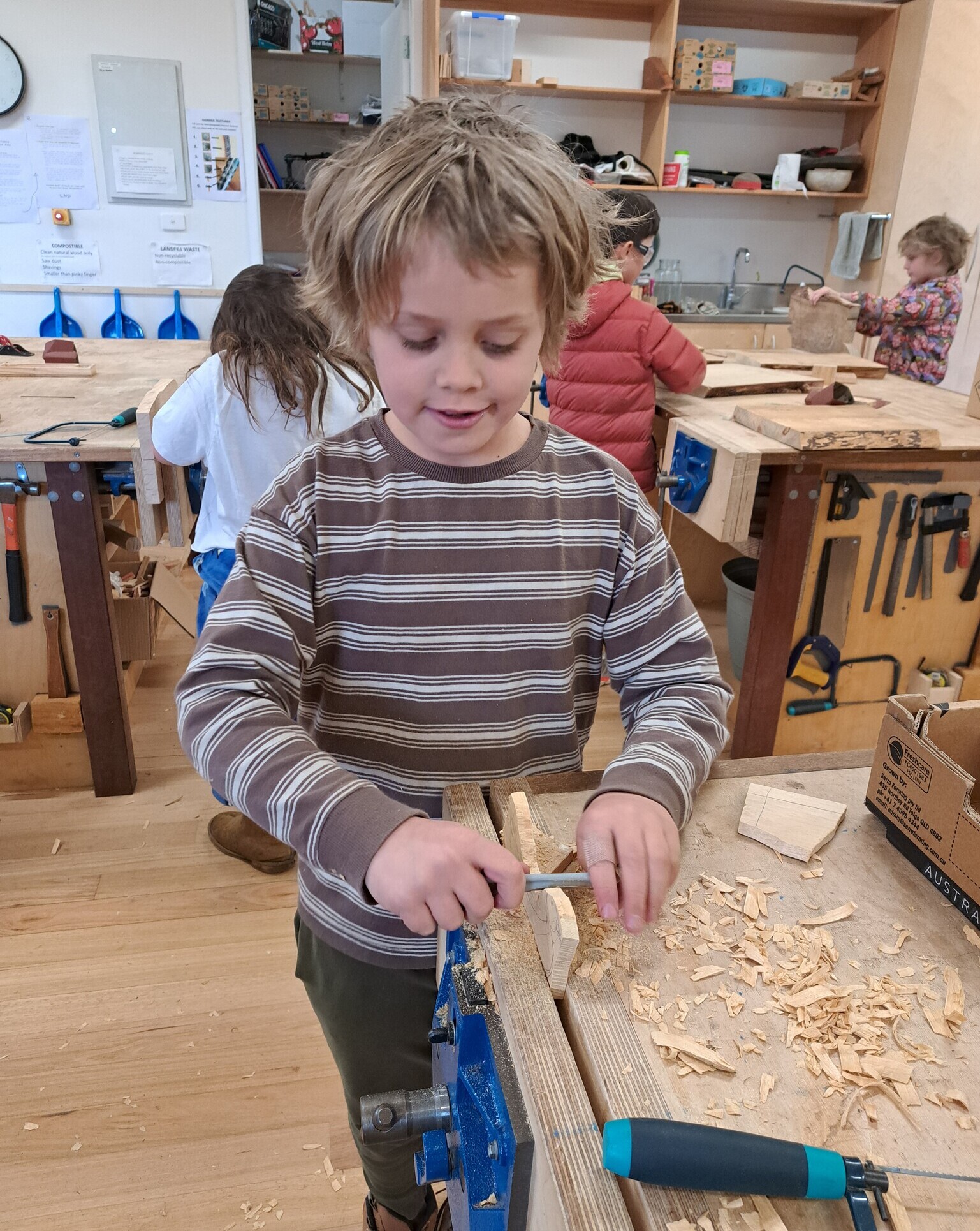 Focused student carves timber at a workbench, connecting head, heart, and hands through purposeful, artistic craftsmanship.