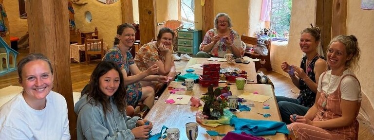 Smiling community members share warmth and connection while hand-crafting together around a communal wooden table at Kindlehill.
